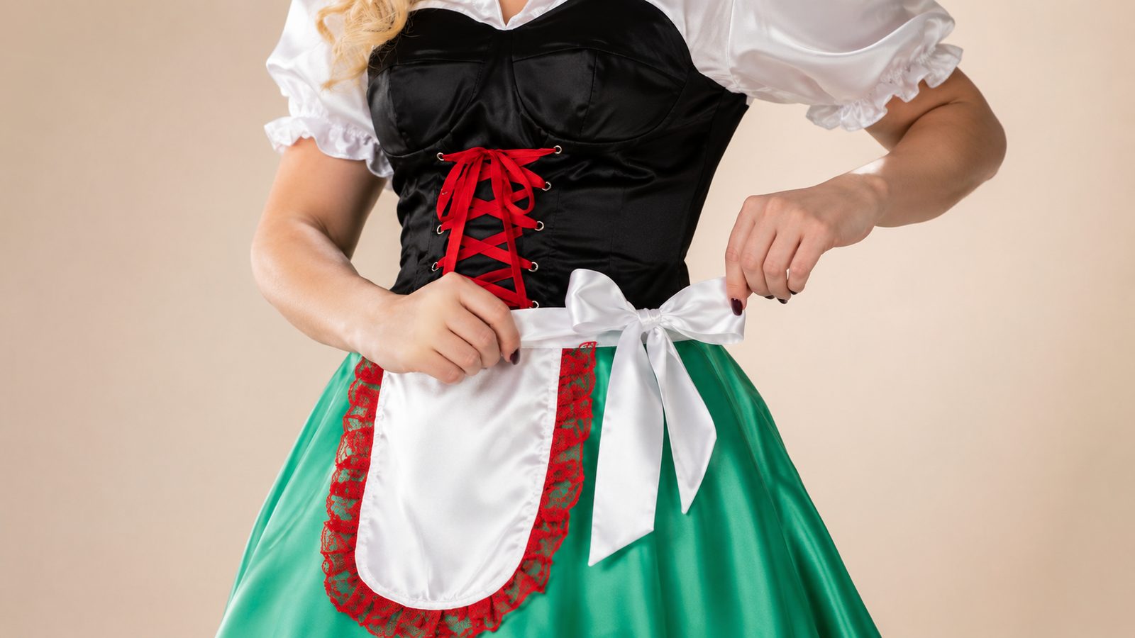 Close detail of a green dirndl with a white lace-trimmed apron tied in a bow at the waist, red corset lacing above