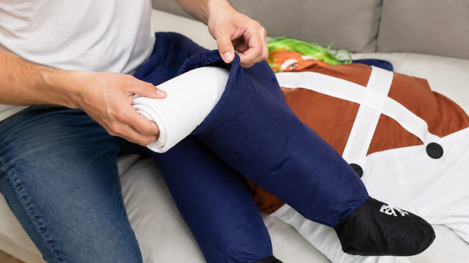 Close-up of an adult stuffing the dangling dummy legs of a plush piggyback costume with a rolled towel to shape the carried illusion