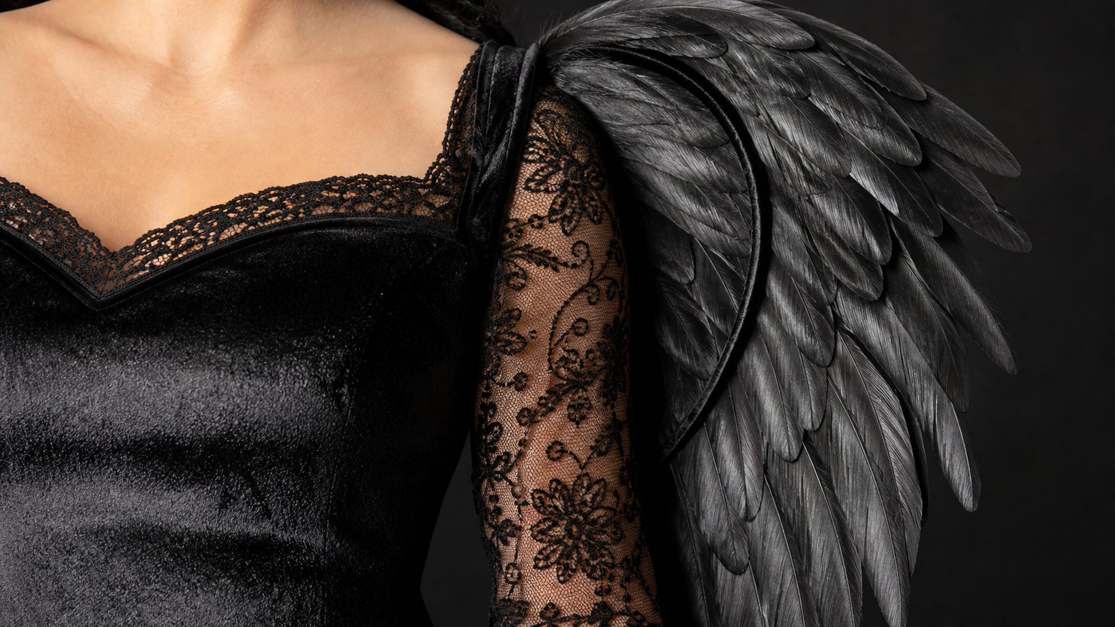Close-up of a black lace dress bodice and the base of a pair of layered black feather-style wings