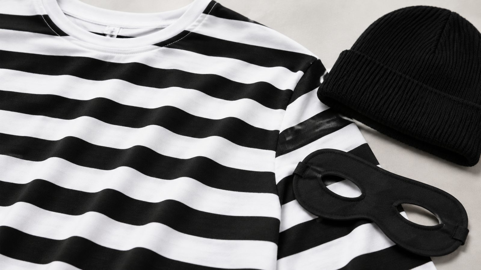 Close-up of black and white striped fabric texture beside a knit beanie and a black eye mask on a plain surface
