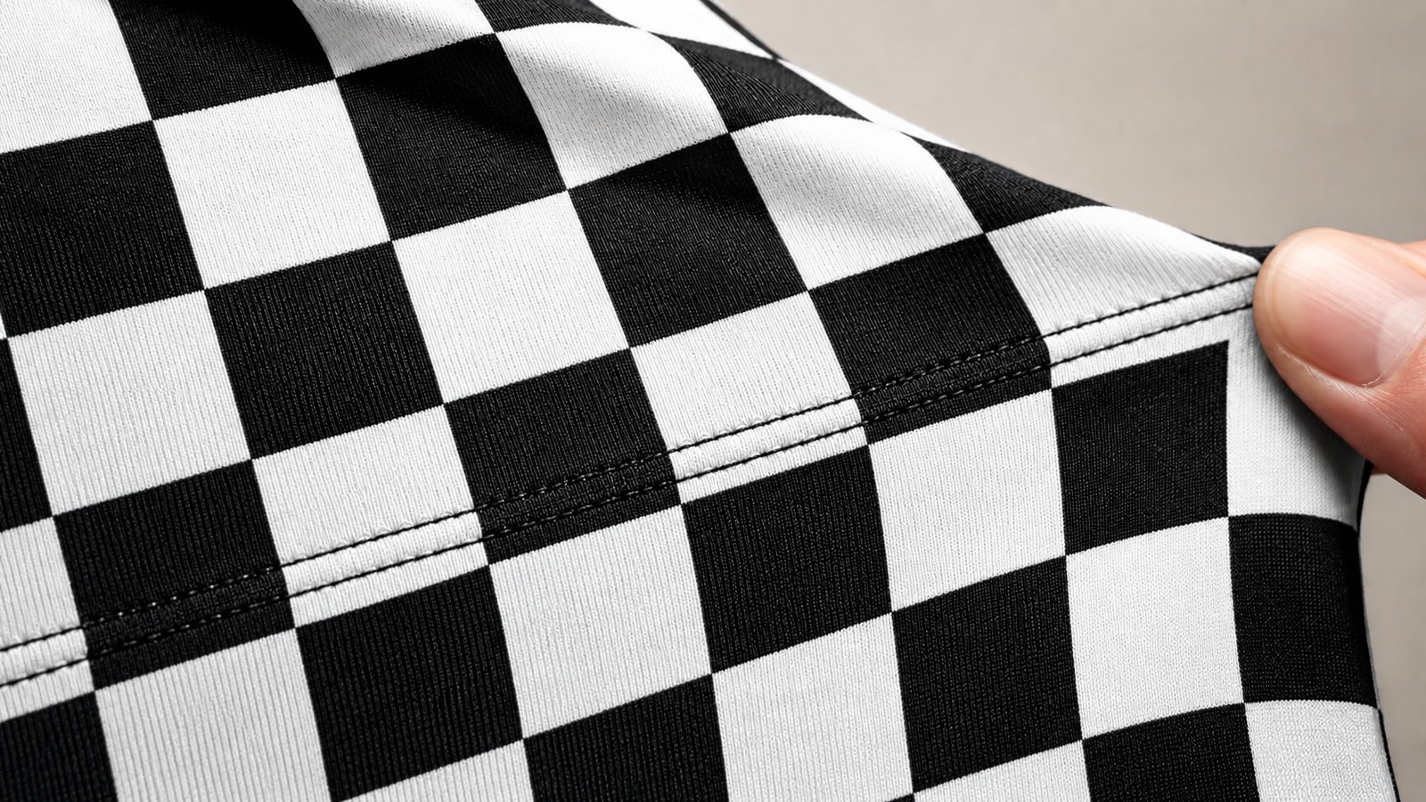 Close-up of black and white checkerboard stretch fabric showing a cover-stitched seam, fabric pulled slightly to show its stretch