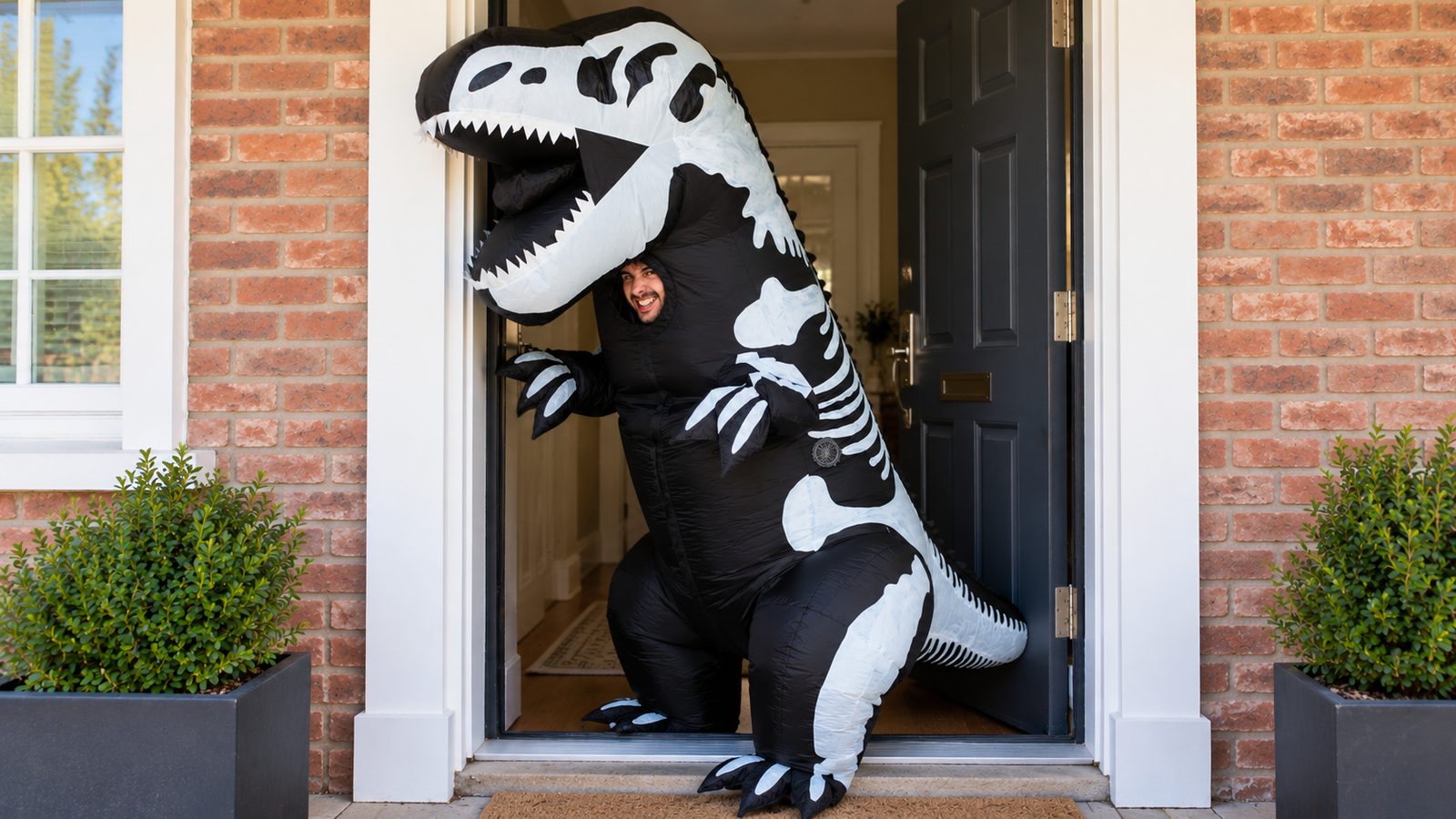 Adult in a black inflatable skeleton dinosaur costume with a white bone pattern turning sideways to fit through a standard front doorway