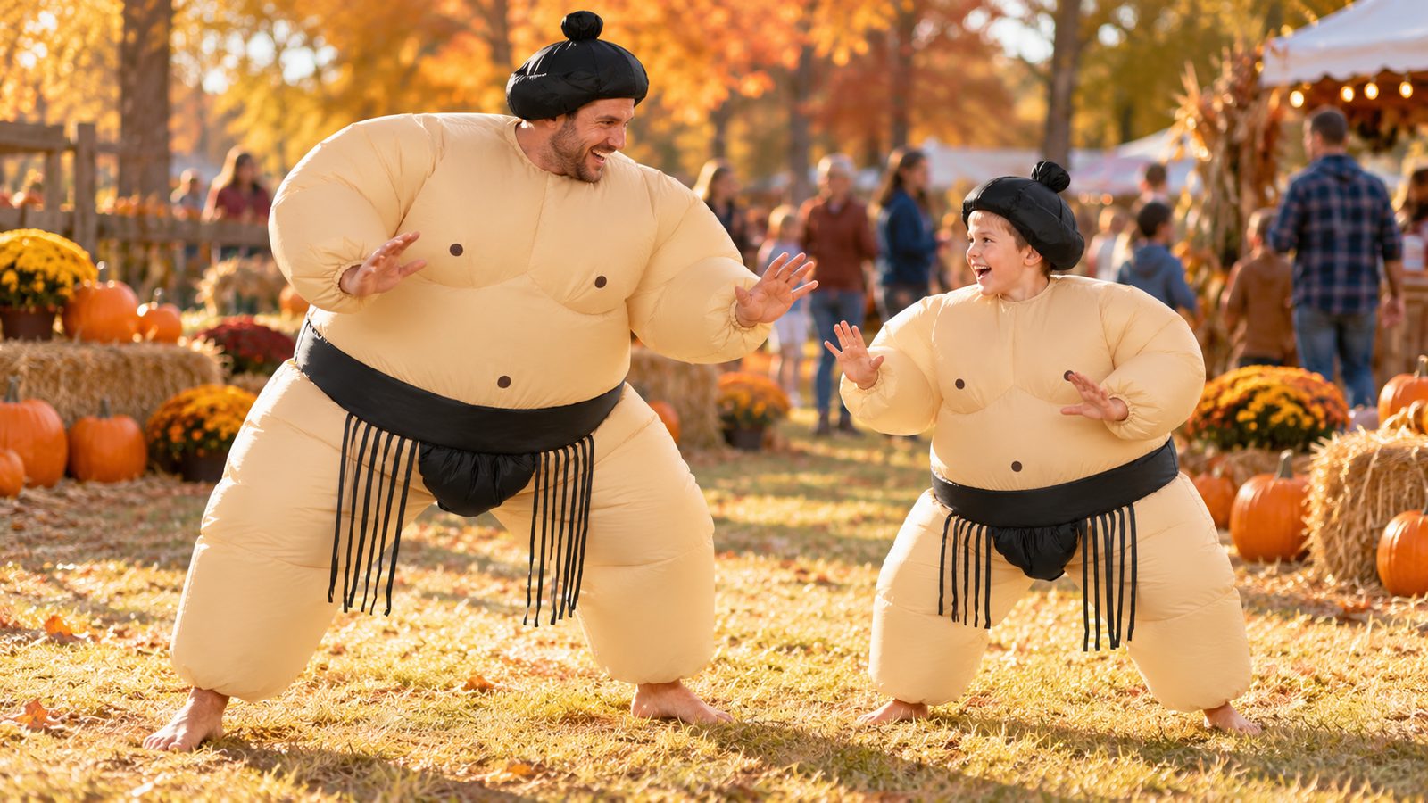 Adult and child in matching black-belt inflatable sumo wrestler costumes squaring off in a playful stance at an outdoor fall festival